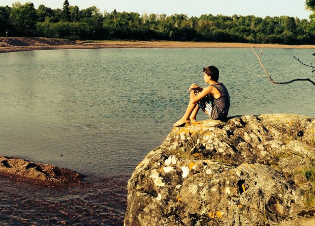 young boy sitting by a lake