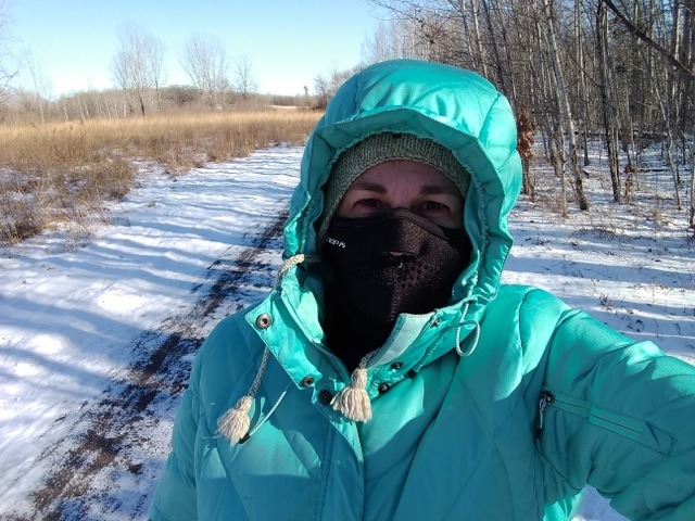 woman bundled up with a down coat, face mask and hat for a winter hike