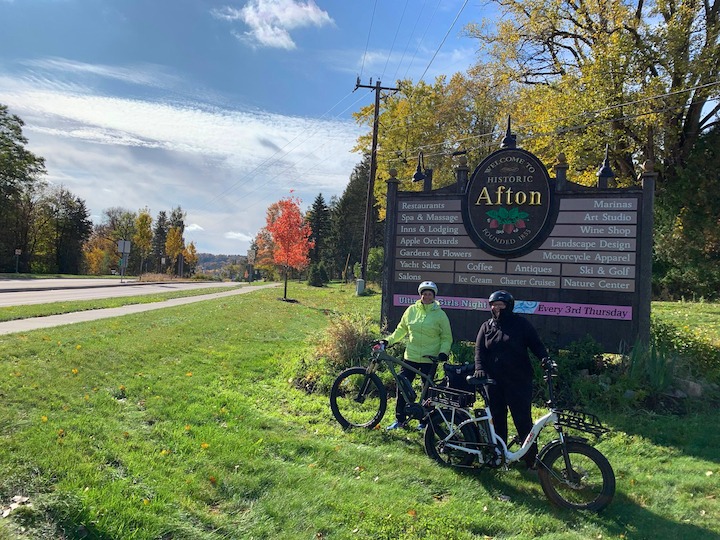 two bikers with electric bikes in front of the Afton city sign