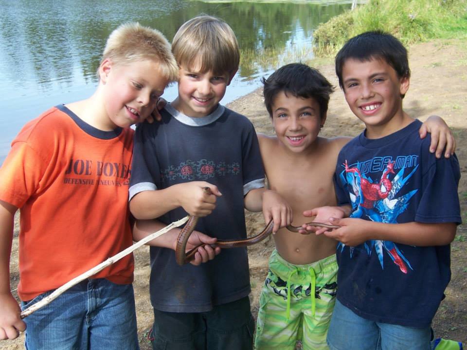 four little boys holding a snake they caught, next to a lake