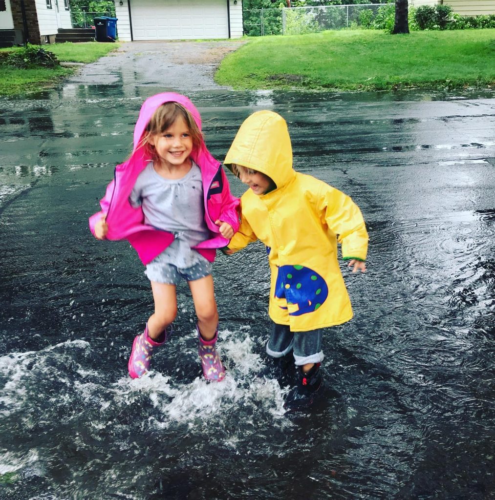 two young kids splashing in a rain puddle