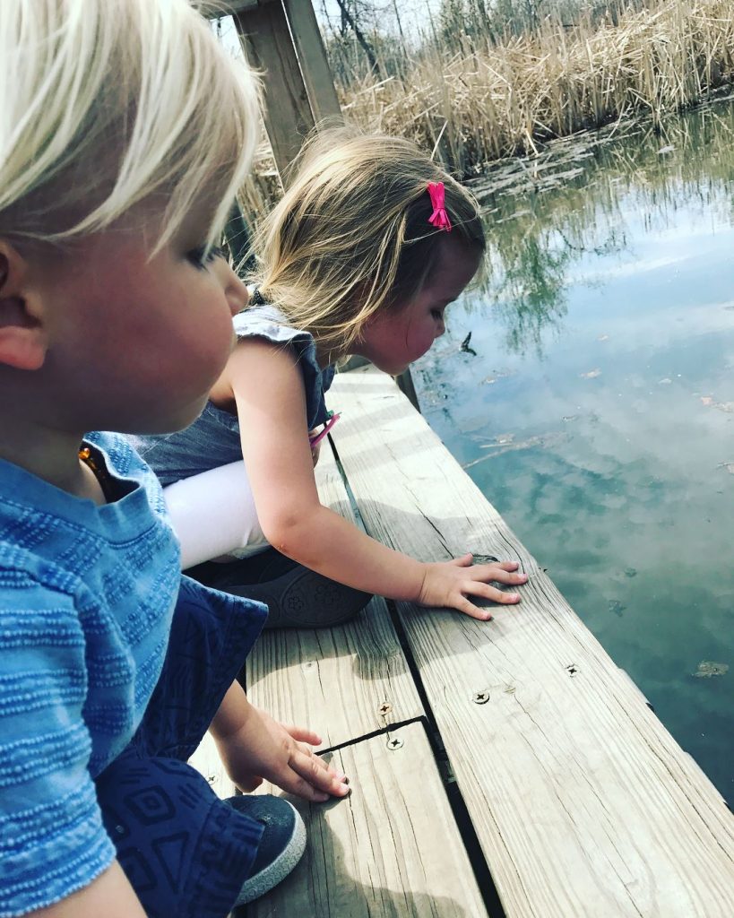 two young children peer into a pond