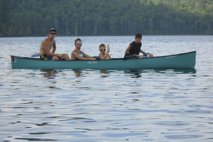 four young men in a canoe on a lake