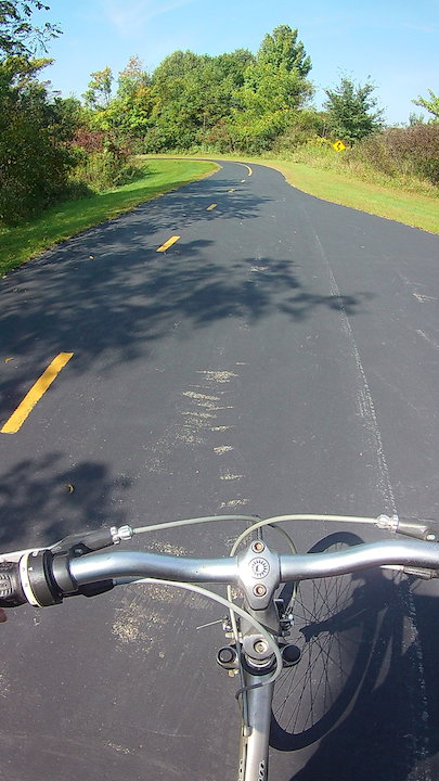 looking over the handlebars to a paved bike trail
