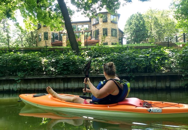 a kayaker looks at a big house while paddling mpls chain of lakes