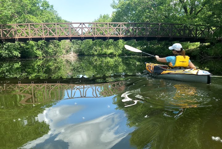 woman kayaking on keller creek, about to go under a foot bridge