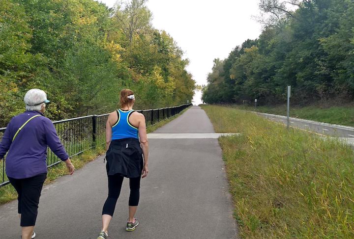 two women hiking uphill on a paved trail