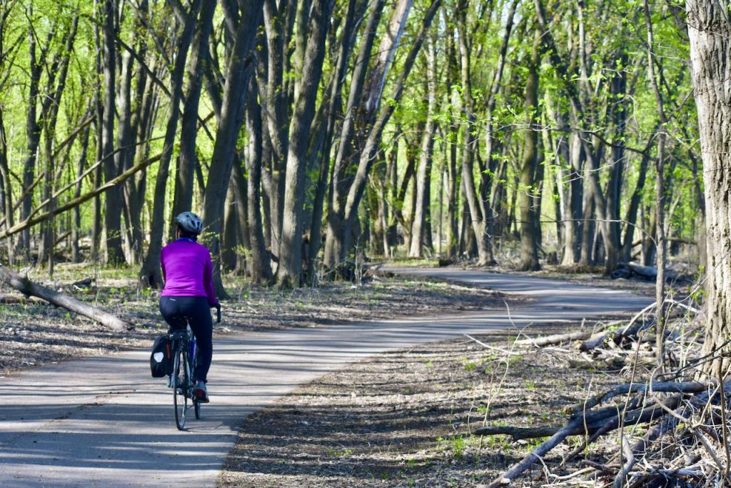 woman biking on a paved wooded trail in crosby farm regional park