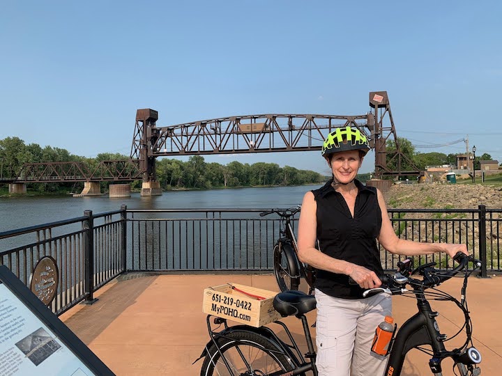 woman with a bike next to the mississippi river with a lift bridge in the background