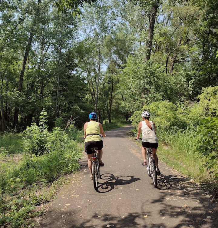 two women biking together on a paved trail through the woods
