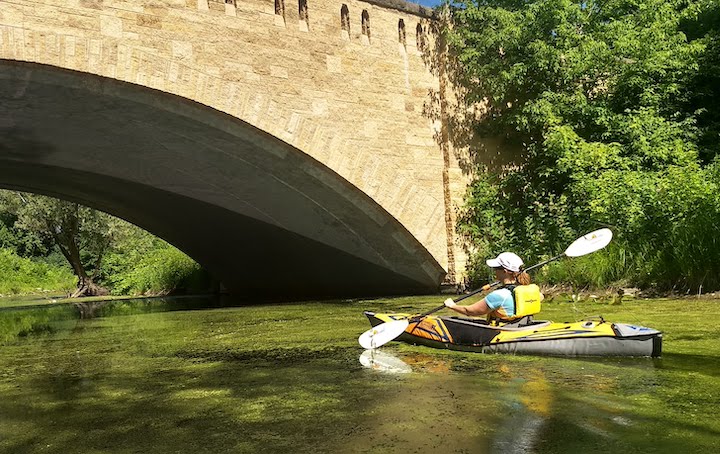 kayaker paddling under a stone bridge