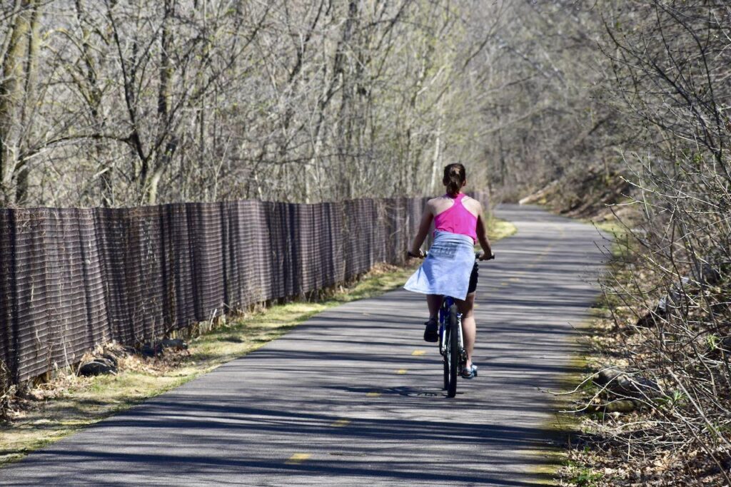 woman biking on brown's creek state trail in the spring, as trees are budding