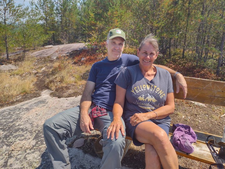 man and wife sitting on a bench on a hiking trail; woman wearing Armachillo Cooling Shorts in navy
