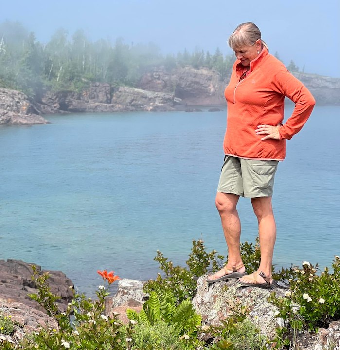 woman in orange top and Kuhl Freeflex cargo shorts in sage, looking at orange lilies with lake in the background