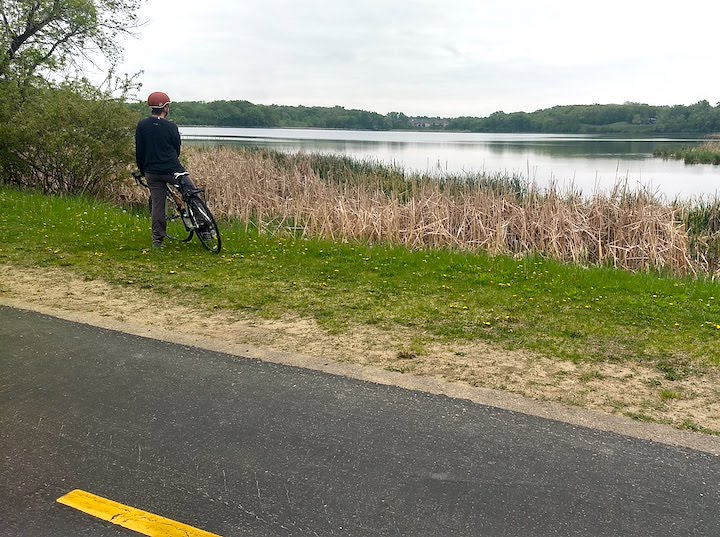 woman with a bike, stopped off the trail and looking over a lake