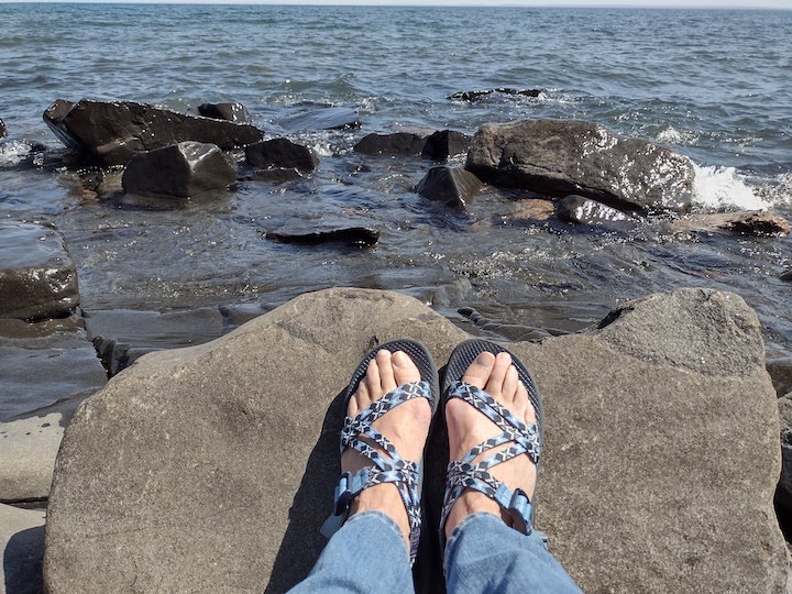feet with double-strap blue chacos; resting on a lakeside rock