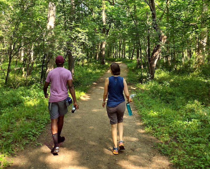 a man and a woman hike on a dirt trail through the woods