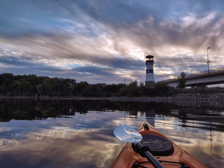 kayaker on a river at sunset, lighthouse and bridge in the background