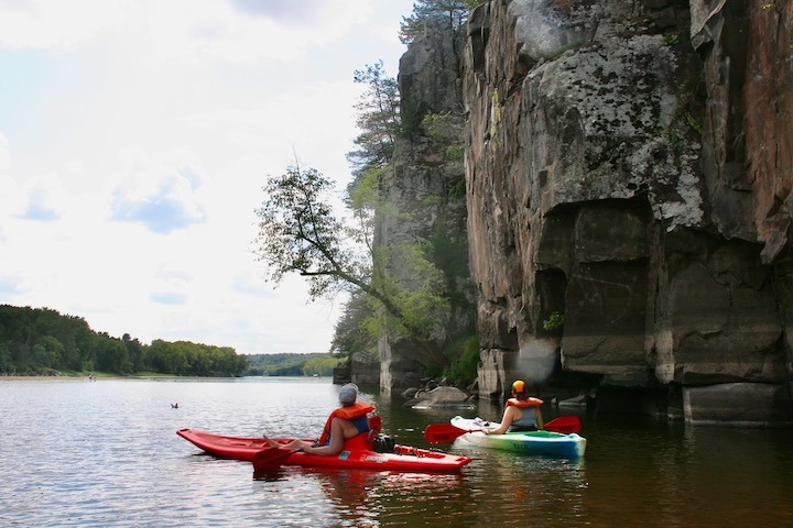 two women kayak alongside a cliff