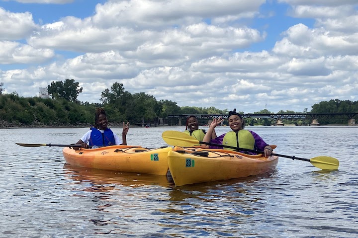 three young women are all smiles in their kayaks on the river