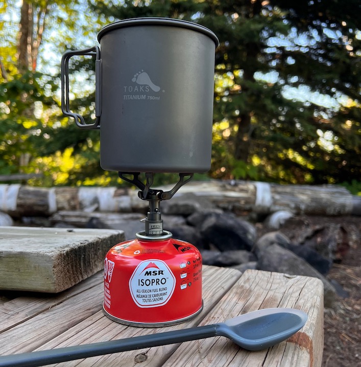 backpacking stove with cookpot on top, sitting on a picnic table