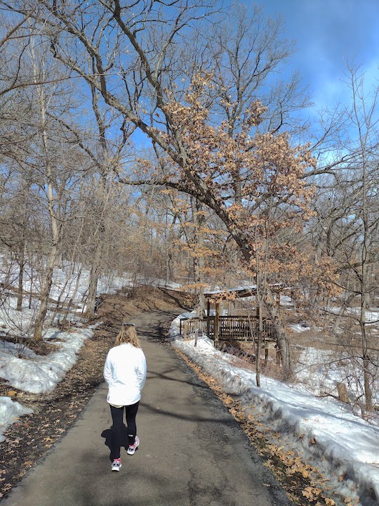 woman walking on a paved trail through the woods in early spring