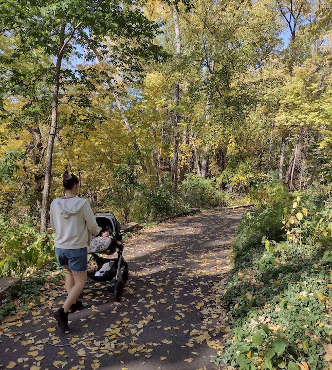 young mom and her baby in a stroller hiking a paved trail in autumn