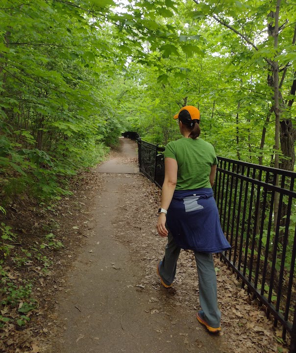 woman hikes the paved trail section with an iron guardrail on the river side