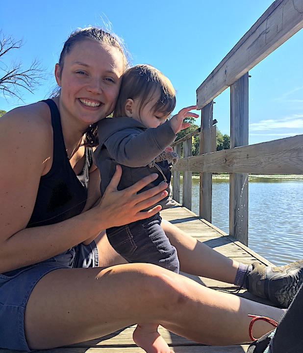 young mom with her baby sitting on a boardwalk at a lake