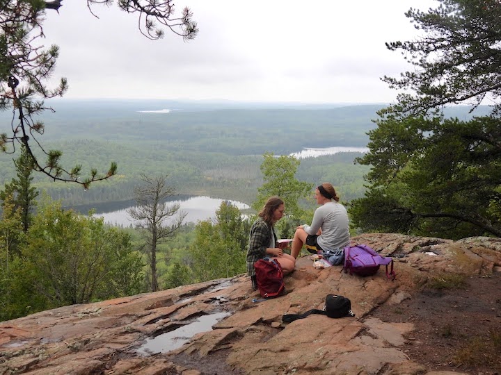 two women rest near the summit of Eagle Mt, overlooking the forests and lakes of the BWCAW